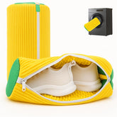 Yellow travel shoe bag with green accents containing white shoes, next to a black suitcase handle.
